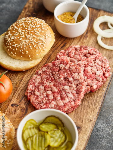 The raw ingredients for the homemade burger. Burger patties. Raw mince meat cutlet, ground beef and pork with bun. Grey background.