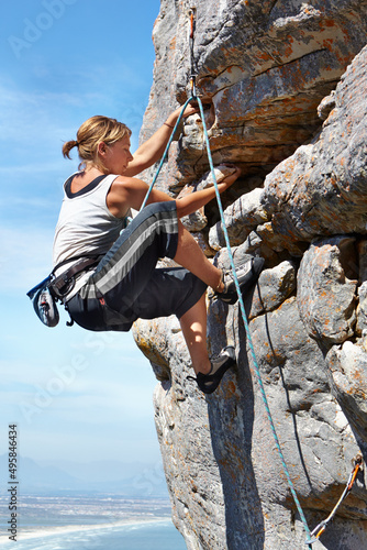 Adrenaline is pushing her to the summit. A young woman climbing up a rock face while framed against a blue sky.