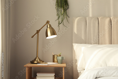 Фототапет Stylish golden lamp and stationery on wooden nightstand in bedroom