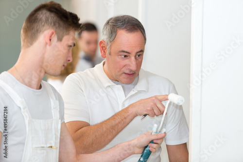 supervisor talking to apprentice using paint roller