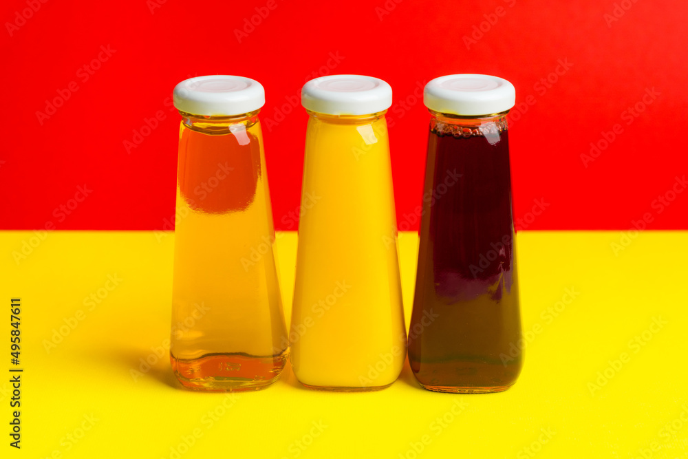 Bottles with yellow and red liquid halthy beverage on yellow background. Orange apple cherry juice Bottles with yellow and red liquid halthy beverage on yellow background. Orange apple cherry juice