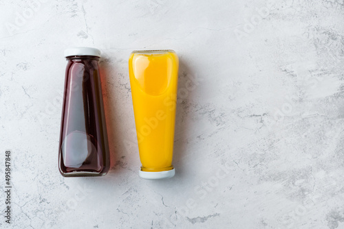 Bottles with yellow and red liquid halthy beverage on gray background. Orange and cherry juice