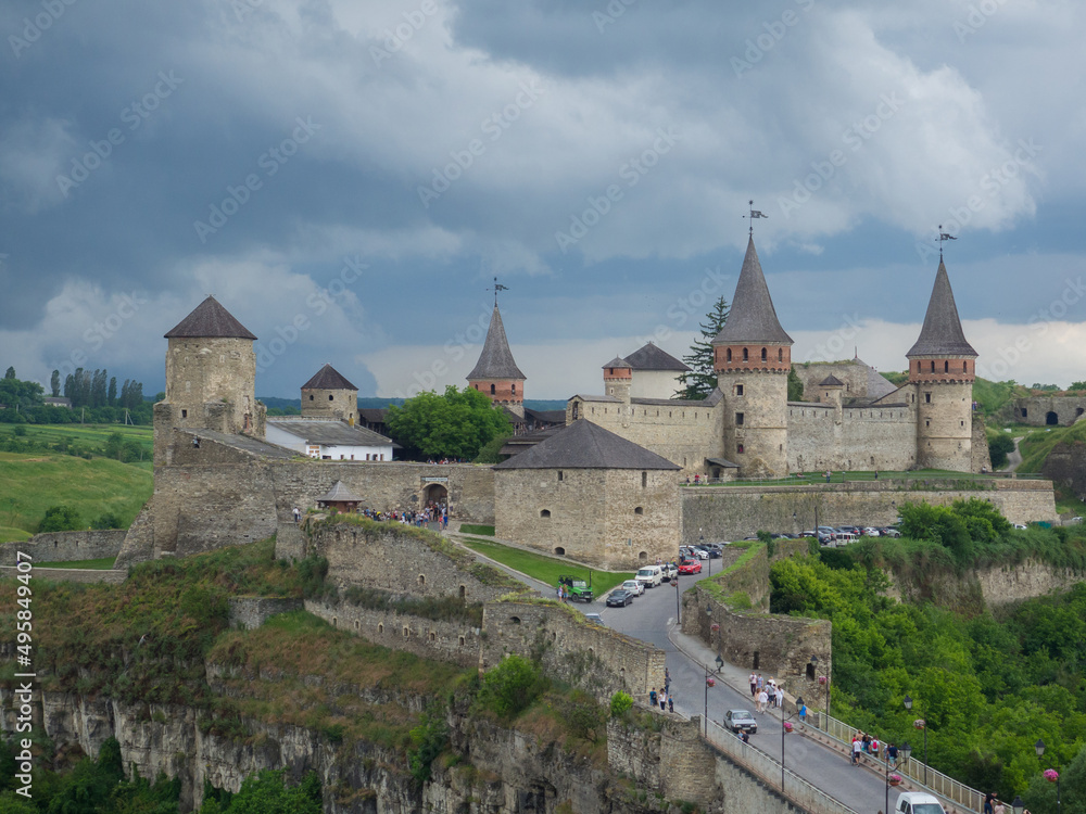 Kamianets Podilsky fortress on cloudy summer day. Scenic summer view of ancient fortress castle in Khmelnytskyi Region, Ukraine. Medieval stone large castle fortress with spiers and defensive towers. Kamianets Podilsky fortress on cloudy summer day. Scenic summer view of ancient fortress castle in Khmelnytskyi Region, Ukraine. Medieval stone large castle fortress with spiers and defensive towers.