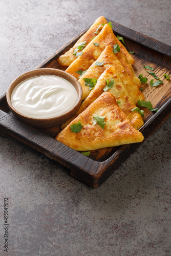 Triangular fried pancakes with meat served with sour cream close up on a wooden tray on the table. Vertical