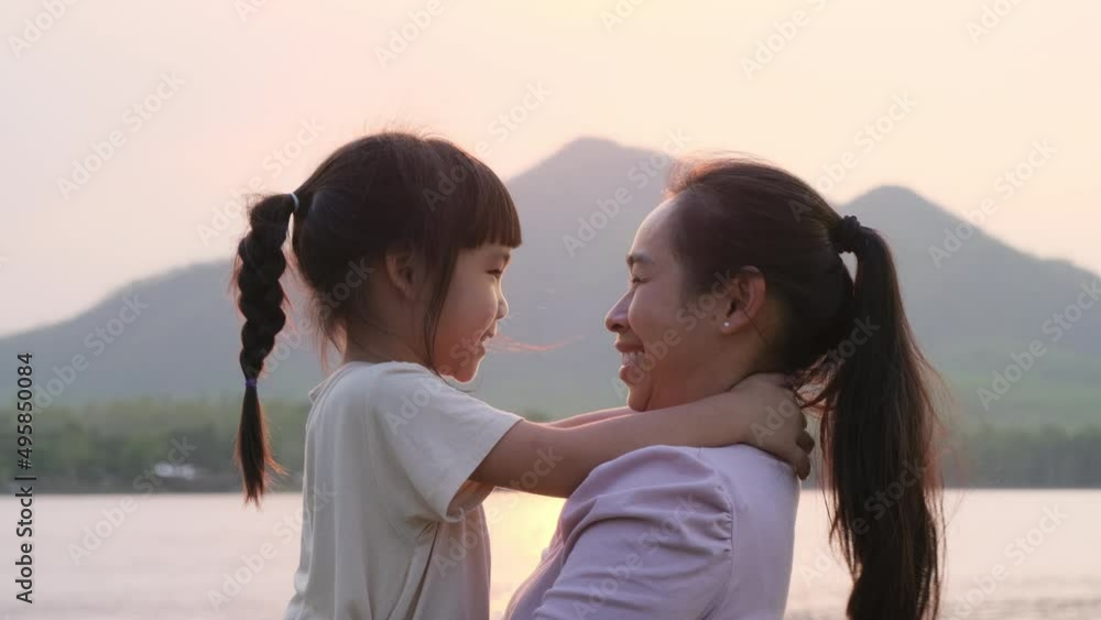 Mother holding a cute little daughter walking by the lake at sunset. Excited kid girl laughs playing with her mother outdoors. Mother hugging her daughter. Mother holding a cute little daughter walking by the lake at sunset. Excited kid girl laughs playing with her mother outdoors. Mother hugging her daughter.