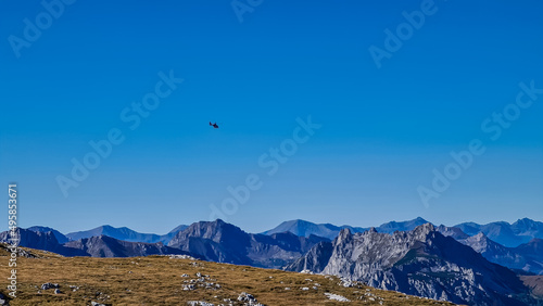Rescue helicopter flying over the mountain peaks of Hochschwab Region in Upper Styria, Austria. Cloudless weather on a sunny summer day in the Alps. Blue misty valley and soft hills. Concept freedom