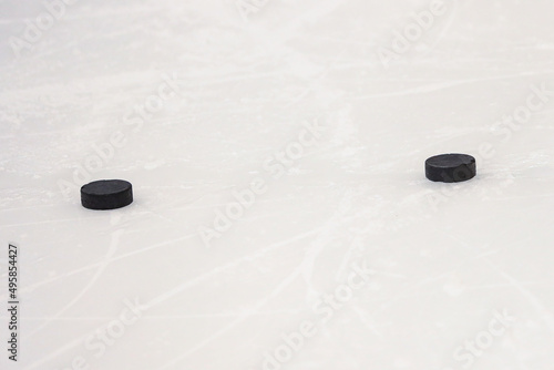 Two black pucks laying on ice hockey rink.