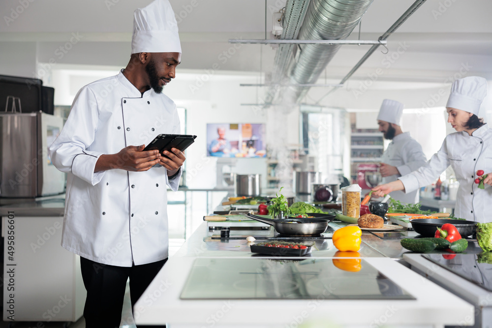 Head cook with tablet brainstorming garnish ideas for gourmet cuisine meal. Food industry worker with handheld touchscreen device preparing ingredients for evening dinner service at restaurant.
