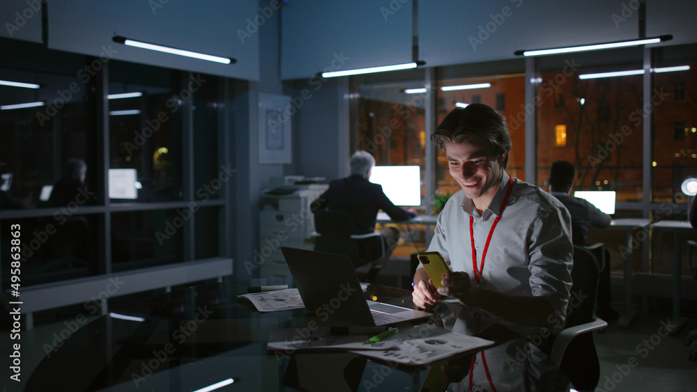 Young businessman work on laptop and receive good email on cellphone working late Young businessman work on laptop and receive good email on cellphone working late