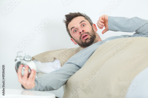 man in bed looking in shock at time on clock