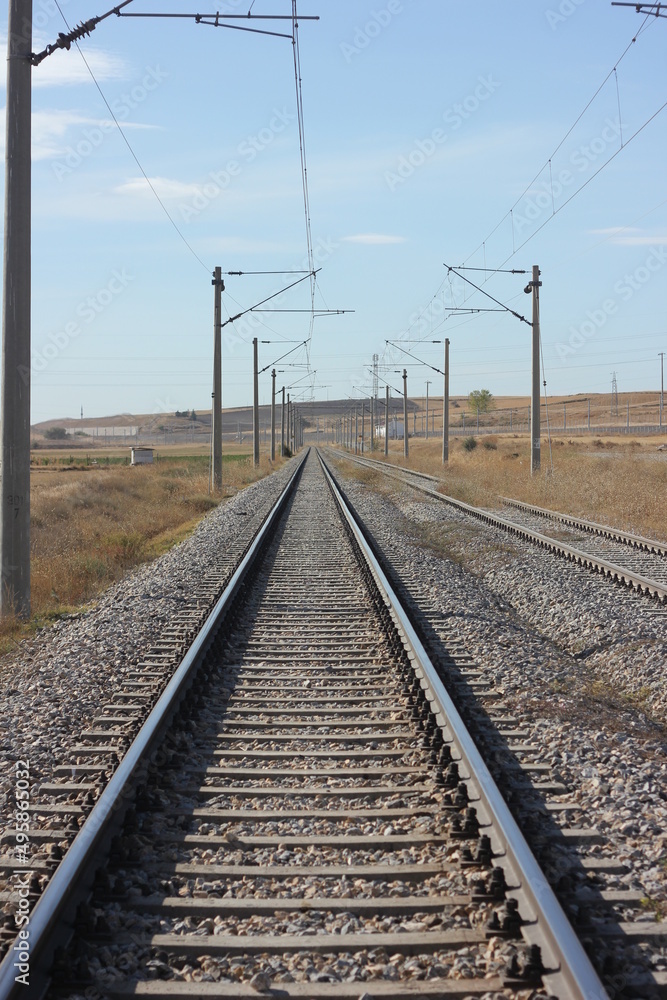 Fototapeta premium Inside of vintage railroad tracks, steel railway for trains, railroad without train, sunny day and clear skies on railway line with electric poles and cable lines