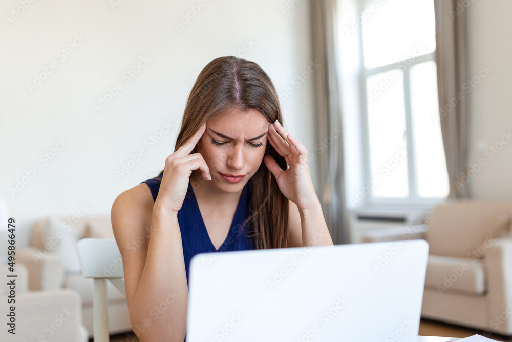 Young frustrated woman working at office desk in front of laptop suffering from chronic daily headaches, treatment online, appointing to a medical consultation, electromagnetic radiation, sick pay Young frustrated woman working at office desk in front of laptop suffering from chronic daily headaches, treatment online, appointing to a medical consultation, electromagnetic radiation, sick pay