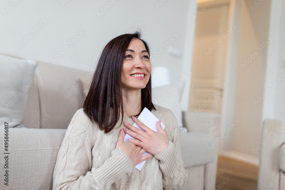 Cheerful Asian woman presses received letter to the chest, at homer, receiving invitation or good news about approved loan, mortgage, tax, insurance, getting notice about acceptance of statement Cheerful Asian woman presses received letter to the chest, at homer, receiving invitation or good news about approved loan, mortgage, tax, insurance, getting notice about acceptance of statement