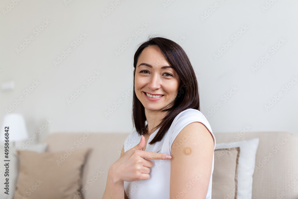 Woman pointing at her arm with a bandage after receiving the covid-19 vaccine. Asian woman showing her shoulder after getting coronavirus vaccine Woman pointing at her arm with a bandage after receiving the covid-19 vaccine. Asian woman showing her shoulder after getting coronavirus vaccine