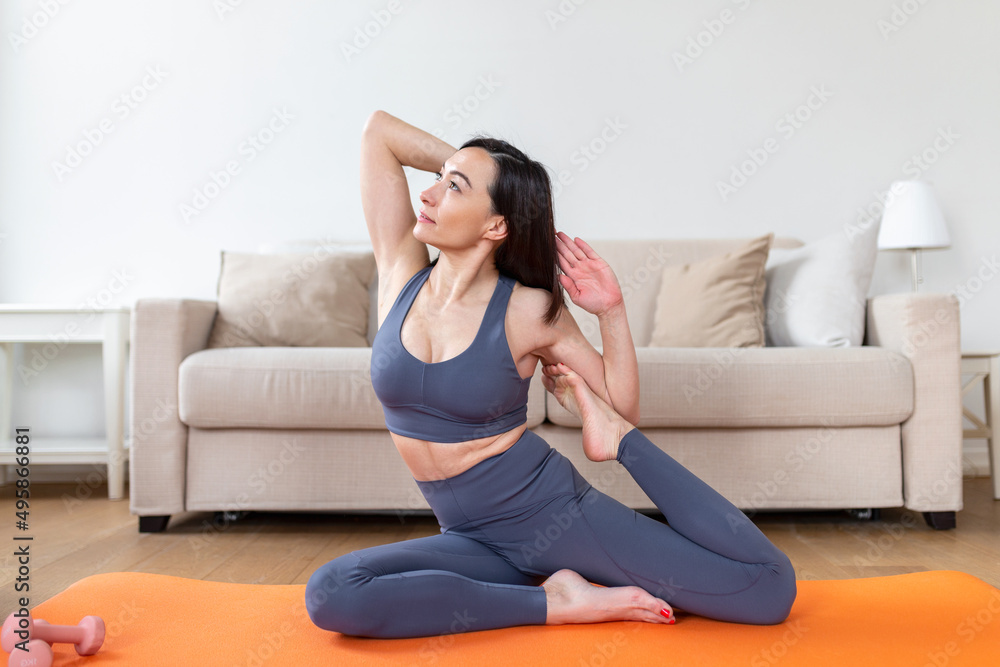Young attractive smiling woman practicing yoga, sitting in Mermaid pose, working out, wearing sportswear, meditation session, indoor full length, home interior Young attractive smiling woman practicing yoga, sitting in Mermaid pose, working out, wearing sportswear, meditation session, indoor full length, home interior