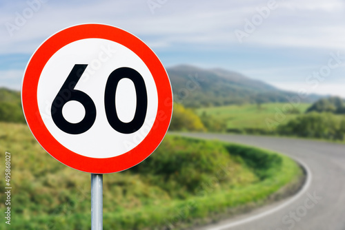 Speed limit sign with curvy road behind. Maximum sixty kilometers per hour. Safety on road background. White round sign red border line. Traffic ticket background. Speeding fine. Slow down on turn. photo