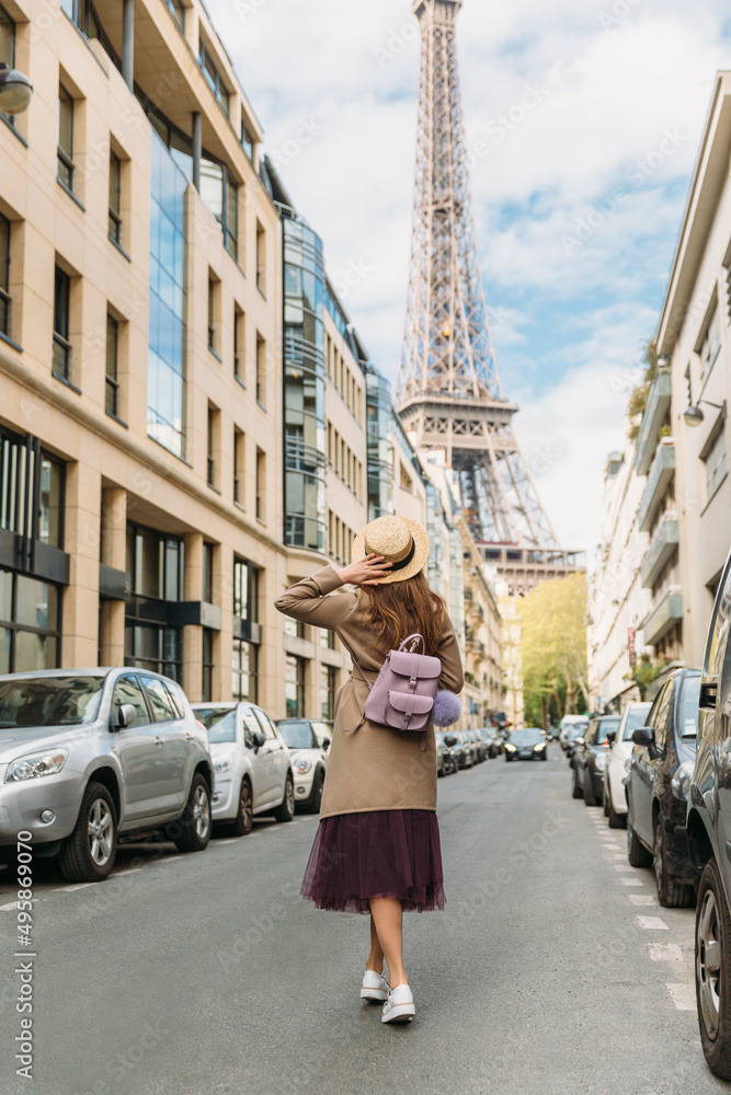 Girl in hat, beige coat and violet backpack looking on Eiffel Tower. Woman travelling by Paris. Wanderlust. Copy space.