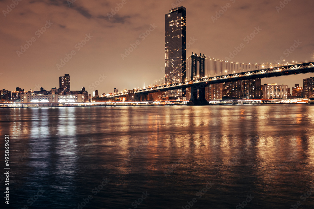 manhattan bridge and new york city skyline at night by the bay