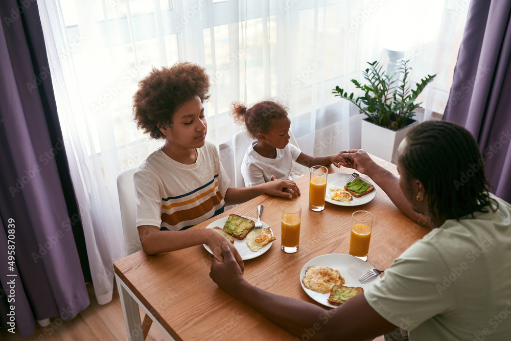 Family hold hands and pray at breakfast at home