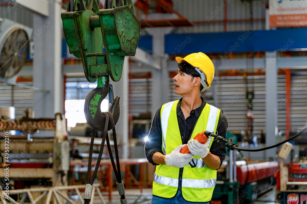 Asian engineer worker is using overhead crane hoist to carry raw