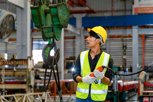 Asian engineer worker is using overhead crane hoist to carry raw materials inside metal sheet manufacturing factory for heavy industrial concept photo