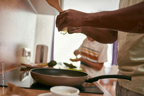 Fototapeta Naklejka Na Ścianę i Meble -  Man breaking egg on pan near son making sandwich
