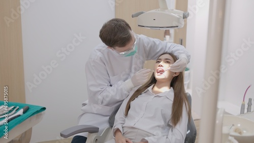 In a dental clinic, a side view of a dentist in uniform treating the teeth of a female patient with a mirror.  photo