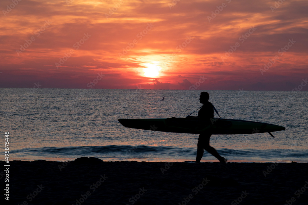 silhouette of a surfer on a red-orange background. Beautiful sunrise on the seaside