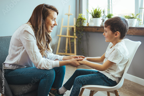 Shot of a little boy talking to a psychologist. Attentive and sympathetic woman psychologist listens to little boy. Notes to himself in clipboard. Mental health. photo