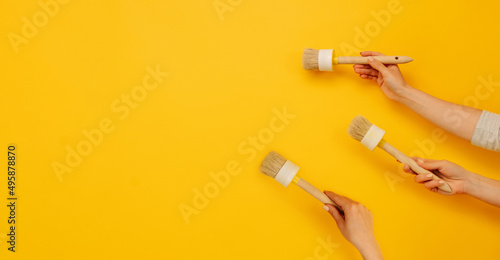 Three hands holding paint brushes on yellow background with copy space. Concept of creativity, improvement and renovation. Working tool