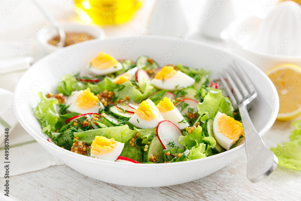 Easter fresh vegetable salad with boiled egg, radish and cucumber, dressing with dijon mustard and lemon on white wooden table Easter fresh vegetable salad with boiled egg, radish and cucumber, dressing with dijon mustard and lemon on white wooden table