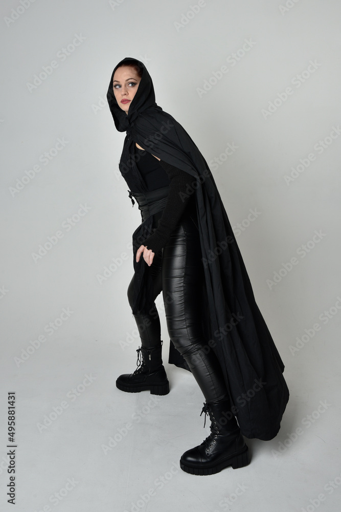 Full length portrait of pretty red haired female model wearing black futuristic scifi leather costume with black flowing cloaked cape. Dynamic standing poses with gestural hands, facing backwards away