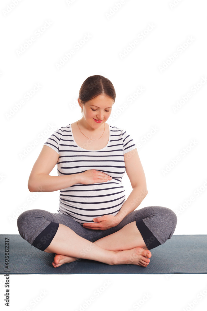 Pregnancy yoga exercise - pregnant woman doing asana Sukhasana easy yoga pose embracing her belly isolated on white background