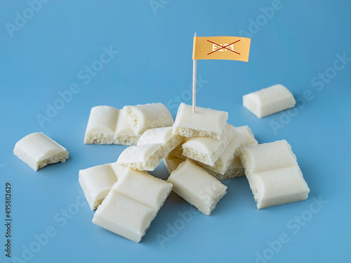 Heap of white chocolate cubes with the sign of a dangerous additive e171 on a blue background photo