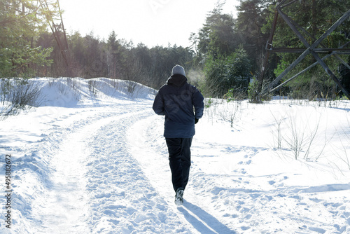 Man runs in the winter along a wide forest road lit by bright sunlight.