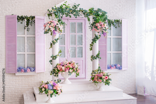 facade of a white and lilac building with a porch decorated with flowers. Photo zone in the photo studio