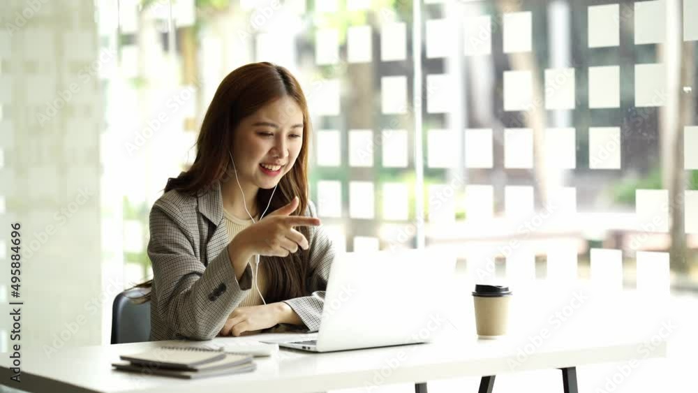 Smiling Asian woman in headphones wave greet to camera talking on video call on laptop. Happy young female in earphones have webcam digital conference or meeting on computer. Smiling Asian woman in headphones wave greet to camera talking on video call on laptop. Happy young female in earphones have webcam digital conference or meeting on computer.