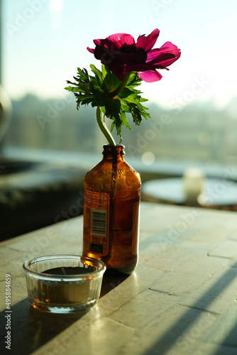 A single flower in a bottle on a table with a sunsent background, vertical shot.