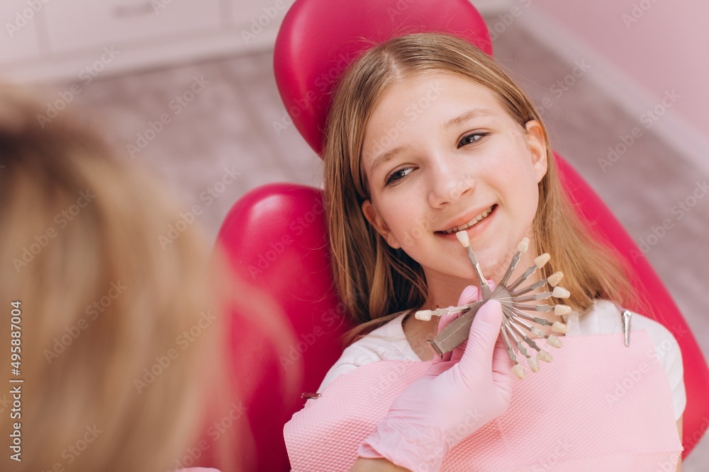 The dentist selects the color of the dental crown of a teenage girl in a dental clinic The dentist selects the color of the dental crown of a teenage girl in a dental clinic