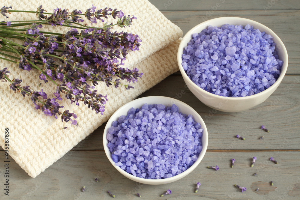 Sea salt with lavender in a white bowls, and lavender flowers on a linen towels are located on a gray wooden table. Closeup. Sea salt with lavender in a white bowls, and lavender flowers on a linen towels are located on a gray wooden table. Closeup.
