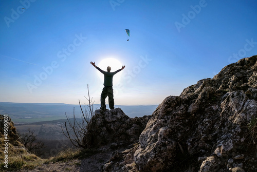 Man alone at mountain top with both arms raised  sun background. Adventure concept