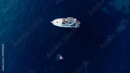 Aerial view of slim woman swimming on the swim ring in the blue sea near yacht in Adriatic sea. Summer seascape with girl, beautiful waves, blue water in sunny day. Top view from drone © nazariykarkhut