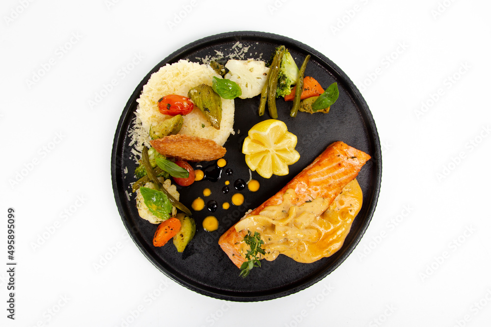 Grilled Salmon with sauteed vegetables and rice cream sauce on black plate Grilled Salmon with sauteed vegetables and rice cream sauce on black plate