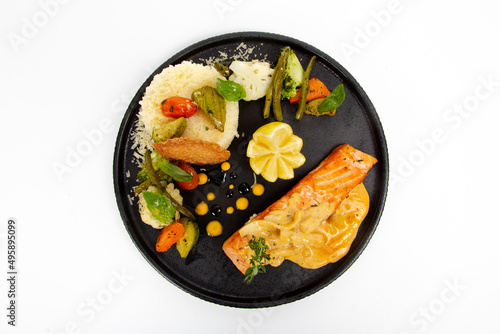 Grilled Salmon with sauteed vegetables and rice cream sauce on black plate