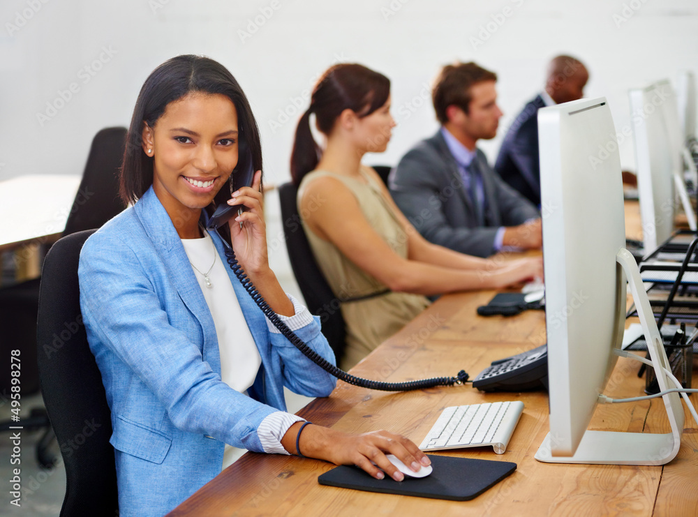 How may I assist you. Portrait of an attractive young woman answering the phone with her colleagues in the background. How may I assist you. Portrait of an attractive young woman answering the phone with her colleagues in the background.