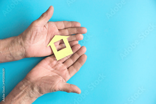 In the hands of an elderly man, a paper-cut house on a blue background. The concept of savings, mortgages and buying an apartment. Right copyspace.