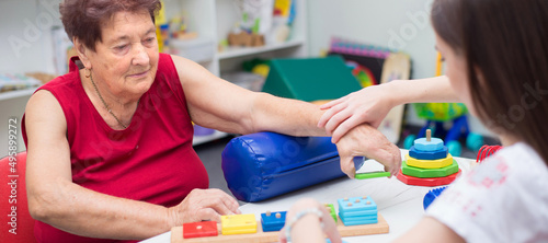 Old woman exercising on physical therapy after stroke with help of physiotherapist in the hospital