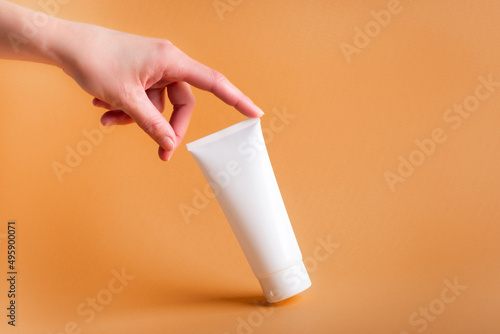 Obraz na płótnie female hand touches a white tube of body cream on an orange background w salonie