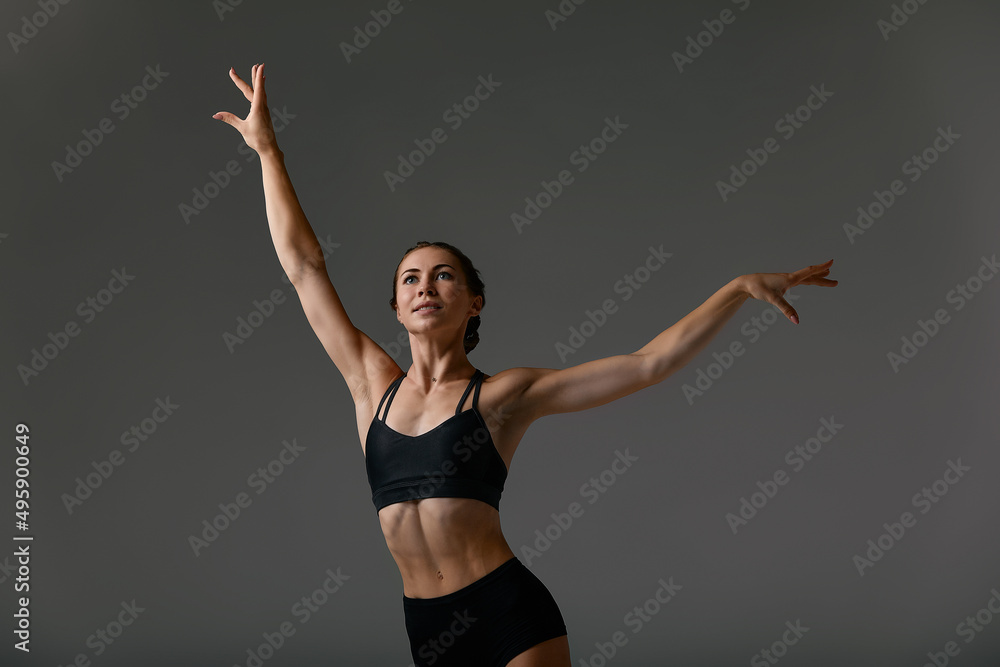 Young attractive gymnastic woman exercise, working out, wearing black sportswear, cool urban style, full length, grey studio background, side view
