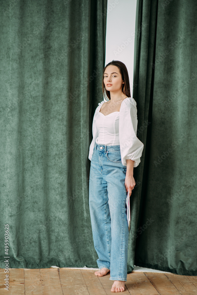 Young brunette woman stands on against curtains background. Young brunette woman stands on against curtains background.